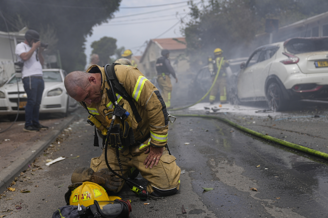 An Israeli firefighter kneels to compose himself Monday after he and his colleagues extinguished cars set on fire by a rocket shot from the Gaza Strip in Ashkelon, Israel. Ohad Zwigenberg/AP